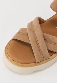 Brown suede sandal with crisscross straps, a smooth leather insole, and a light-colored platform sole. Features visible stitching detail.