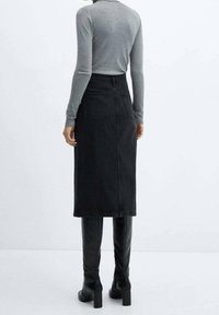 Falda de mezclilla negra con una cintura ajustada, bolsillos traseros y largo midi, combinada con botas negras por encima de la rodilla y una camiseta de manga larga gris.