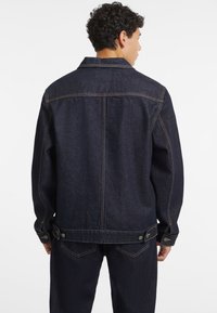 Dark denim jacket featuring a classic design, visible stitching, button accents, and a relaxed fit, shown from the back.