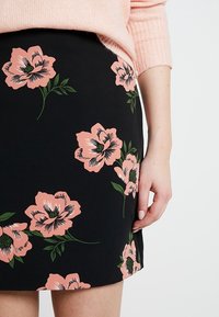 Svart kjol med stora rosa blommiga tryck och gröna stjälkar. Tyget verkar slätt med en rak design och en sidoflik. 