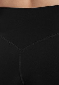 Leggings neri a vita alta realizzati in un tessuto liscio e elastico, con un bordo in vita testurizzato e un dettaglio di cucitura triangolare sul retro.