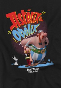 Schwarzes T-Shirt mit den Cartoon-Charakteren Asterix und Obelix, in lebhaften Farben, mit fettem Text und einem verspielten Design. Der Hintergrund zeigt einen kleinen Hund.