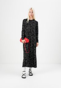Svart langermet kjole med hvit blomsteromrissdesign, kombinert med en rød veske, hvite sokker og svarte sandaler med stropper.