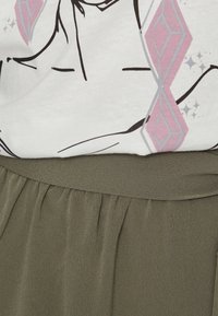 Weißes T-Shirt mit schwarzem Grafikdesign und rosa Akzenten, kombiniert mit einem olivgrünen, strukturierten Rock mit gerafftem Bund.