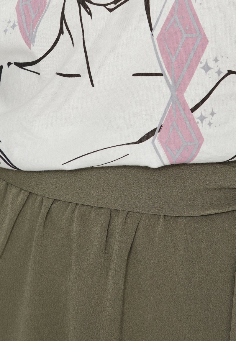 Weißes T-Shirt mit schwarzem Grafikdesign und rosa Akzenten, kombiniert mit einem olivgrünen, strukturierten Rock mit gerafftem Bund.