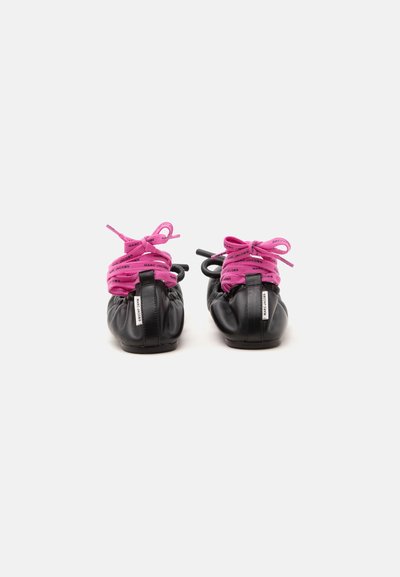 Ballerines en cuir noir avec des lacets rose vif de la marque Marc Jacobs, noués en nœuds, vues de dos sur fond blanc.