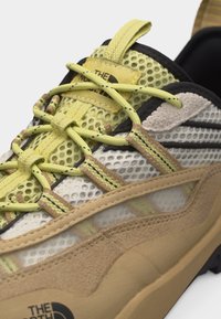 Αθλητικό παπούτσι με κίτρινο κολάρο από πλέγμα, υπερβολές από μπεζ σουέτ, κίτρινες κορδέλες με σχέδιο και λογότυπο "The North Face" στη γλώσσα και την σόλα.