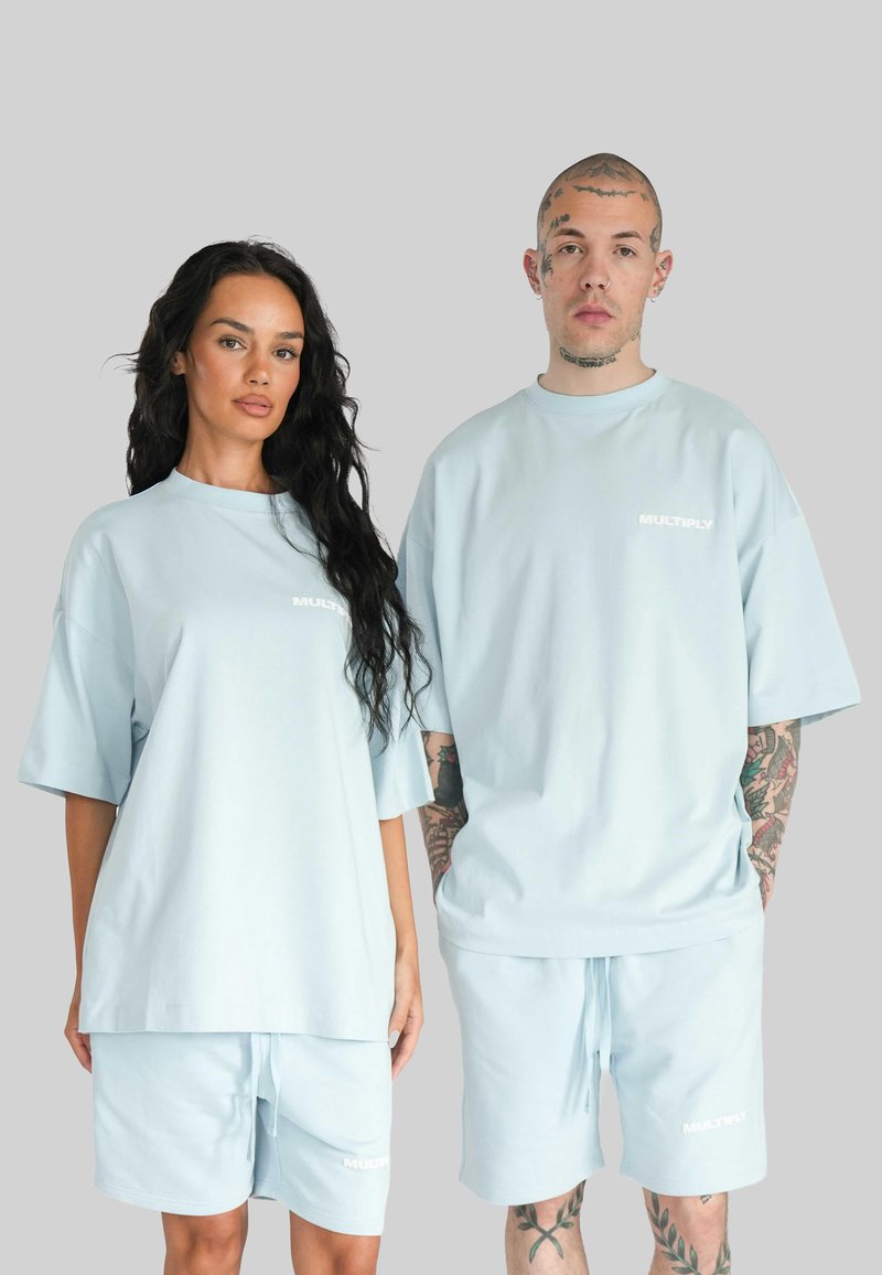 Světle modré bavlněné oversized trička s krátkými rukávy a odpovídajícími šortkami. Na přední straně se nachází bílé logo v oblasti hrudníku. Hladká textura.