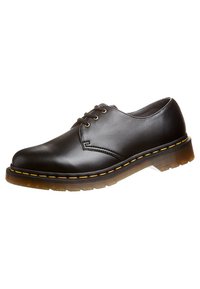 Scarpa nera in pelle con lacci, suola in gomma marrone spessa e cuciture gialle, stile casual, vista angolata su sfondo bianco.
