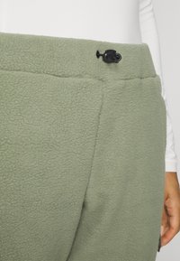 Green fleece pants with a soft texture, featuring a black drawstring at the waist and a simple, smooth design.
