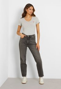 Grey cotton t-shirt with a v-neck and small red triangle logo, paired with high-waisted black jeans and white sneakers. Minimalistic design.