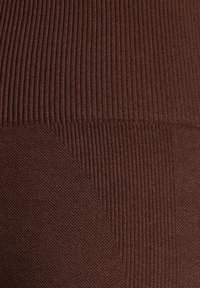 Tessuto a coste marrone con texture variabili; sezioni lisce e testurizzate creano un contrasto. Vista ravvicinata e dettagliata della superficie del materiale.