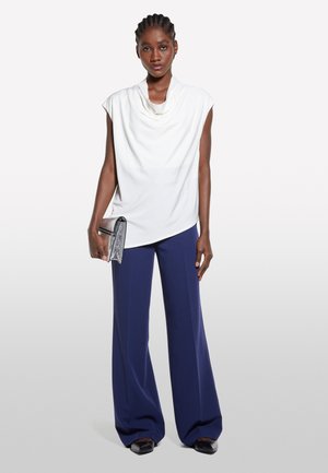 Top bianco con scollo drappeggiato, pantaloni a gamba larga blu navy, pochette argentata. Tessuto morbido, vestibilità comoda e silhouette contemporanea. Scarpe nere.