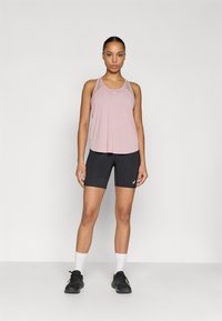 Αθλητική φανέλα σε ανοιχτό ροζ χρώμα με λεπτές τιράντες και χαλαρή εφαρμογή, συνδυασμένη με μαύρα ποδηλατικά σορτς, και τα δύο κατασκευασμένα από ύφασμα που απομακρύνει την υγρασία.