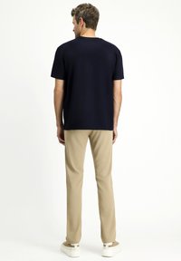 T-shirt blu navy a maniche corte, tessuto morbido, colletto girocollo, abbinato a pantaloni beige e sneakers bianche, visto da dietro.