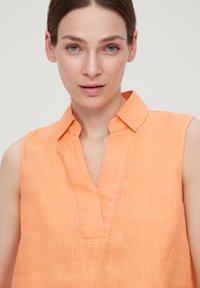 Ärmelloses Top aus leichtem orangen Leinen mit einem Kragen und einem Schlitz an der Vorderseite. Sanfte Textur mit minimalen Nähdetails.