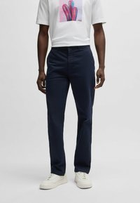 Marineblauwe broek met een rechte snit, gemaakt van lichtgewicht stof. Bevat een platte voorkant en klassieke zakken. Gepaard met witte sneakers.