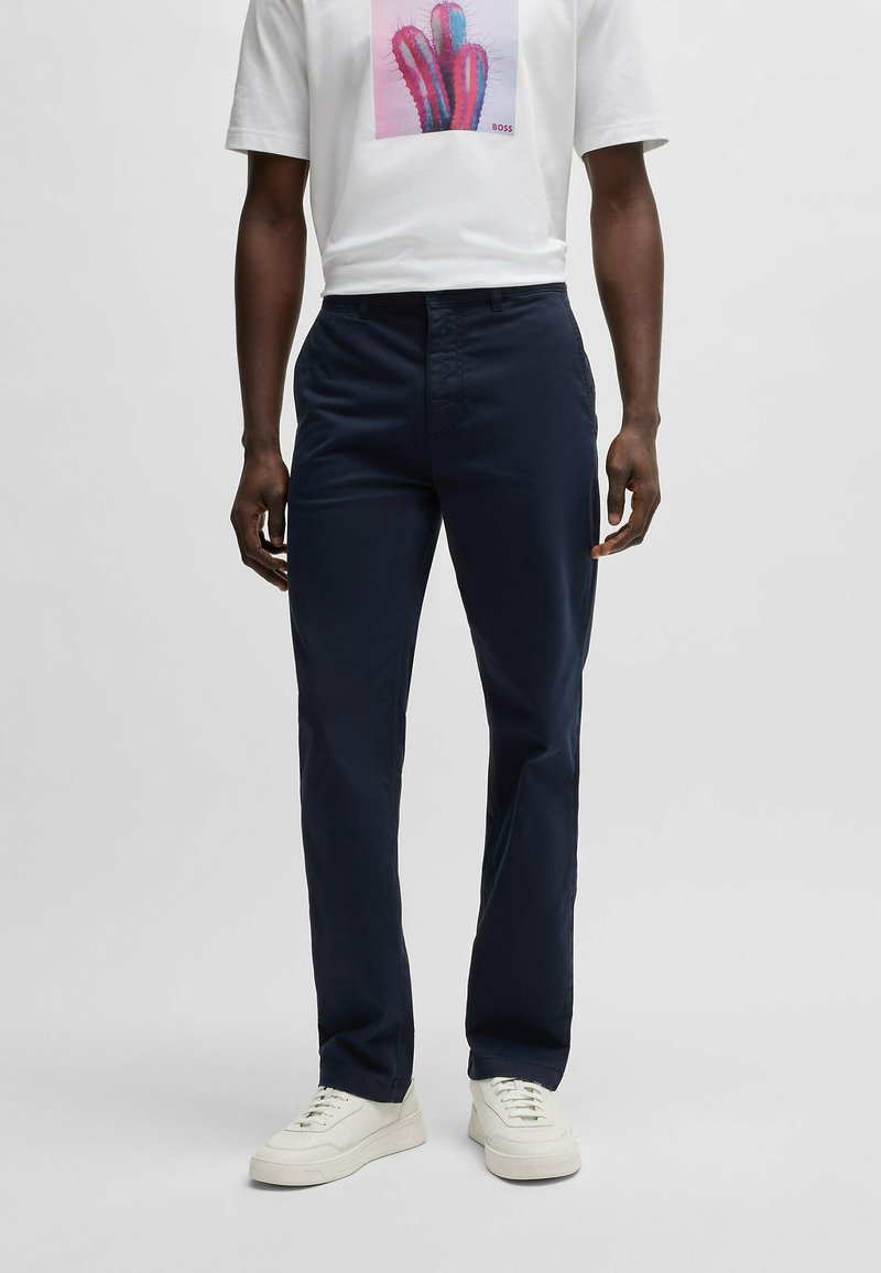 Marineblauwe broek met een rechte snit, gemaakt van lichtgewicht stof. Bevat een platte voorkant en klassieke zakken. Gepaard met witte sneakers.