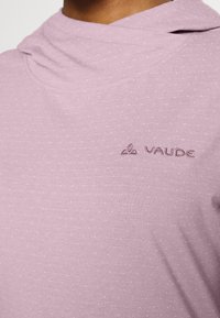 Světle fialová košile s jemnou texturou a tečkovaným vzorem. Obsahuje kapuci a jemně vyšívané logo Vaude na levé straně.
