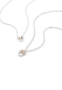 Due collane mostrano catene in argento con un gancio rotondo che presenta un accento a forma di fiocco dorato. Una catena è texture, mentre l'altra è a maglie.