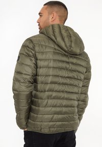 Chaqueta de abrigo verde oliva con capucha, que cuenta con un tejido acolchado y puños elásticos. La parte trasera presenta un acabado suave y un mínimo de marca.