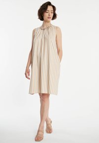 Robe sans manches avec des rayures verticales en crème et marron clair, dotée d'un col froncé et de poches latérales. Texture du tissu lisse.