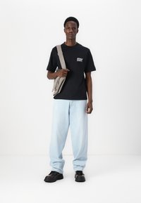 Black short-sleeve t-shirt with white text, light blue loose-fit jeans, and black chunky shoes. Gray shoulder bag with zipper detail.