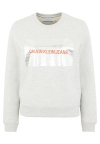 Sudadera de felpa gris claro con mangas largas, cuello redondo y parche rectangular reflectante plateado que muestra "CALVIN KLEIN JEANS" en naranja.