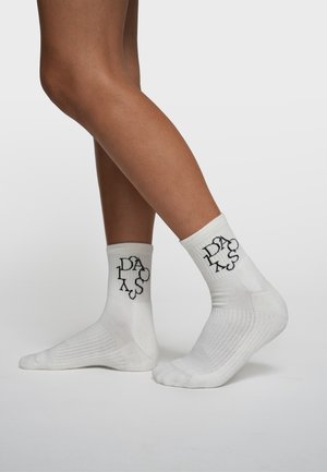 Chaussettes courtes en coton blanc avec un logo imprimé en noir. Le design comprend une texture côtelée et des sections renforcées au talon et aux orteils.