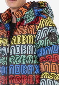 Zwarte pufferjack met een meerkleurig "PONDBAX" tekstpatroon. Heeft een ritssluiting aan de voorkant, een capuchon en een logo-patch op de mouw. Textuurafwerking.