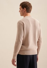 Beiger Rippenpullover mit langen Ärmeln, rundem Hals und elastischen Bündchen, hergestellt aus einem weichen Material. Glatte Textur ohne sichtbare Muster.