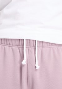 Hellrosa Jogginghose mit elastischem Bund, weißem Kordelzug und kleinen Quasten, glatter Textur und seitlichen Nahtdetails.