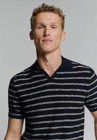 Marineblauwe gestreepte polo met korte mouwen, voorzien van een v-hals ontwerp, dunne witte strepen en een zachte textuur.