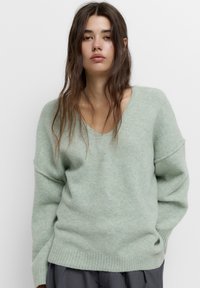Pulover cu decolteu în V, de culoare verde deschis, realizat dintr-un material moale, cu o croială lejeră, umeri lăsați și margine côtelată.
