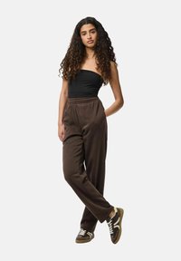 Bruine joggingsbroek met elastische tailleband, gecombineerd met een zwarte strapless top en bruine sneakers met witte accenten. Krullend haar.