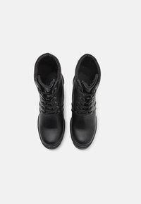 Bottines en cuir noir avec un design à lacets, un col matelassé et un bout rond. Comprend des œillets métalliques et une doublure texturée.