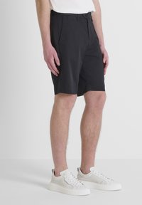 Pantaloni corti neri casual con tasche laterali, materiale leggero, vestibilità su misura e chiusura con bottone, abbinati a sneakers bianche.