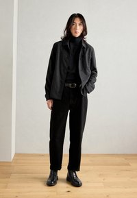 Black wool shirt jacket paired with a black turtleneck, black trousers, and black leather ankle boots. Minimalist design with a textured finish.