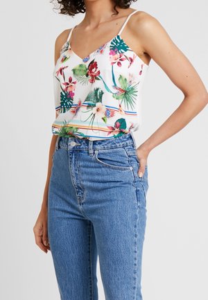 Blomstermønstret cami i hvid med levende tropiske farver og tynde stropper. Kombineret med højttaljede blå jeans.
