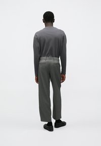 Hosszú ujjú, szürke, testhezálló felső laza szürke nadrággal párosítva. Az öltözéket fekete cipő és minimalista stílus egészíti ki.