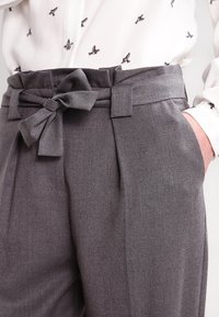 Szare dopasowane spodnie o fakturowanym wykończeniu, z szerokim paskiem z kokardą, plisami i bocznymi kieszeniami. Połączone z białą bluzką w ptasi wzór.