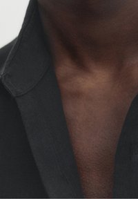 Zbliżenie szyi i górnej części klatki piersiowej osoby o ciemnej karnacji w czarnej koszuli z kołnierzykiem.