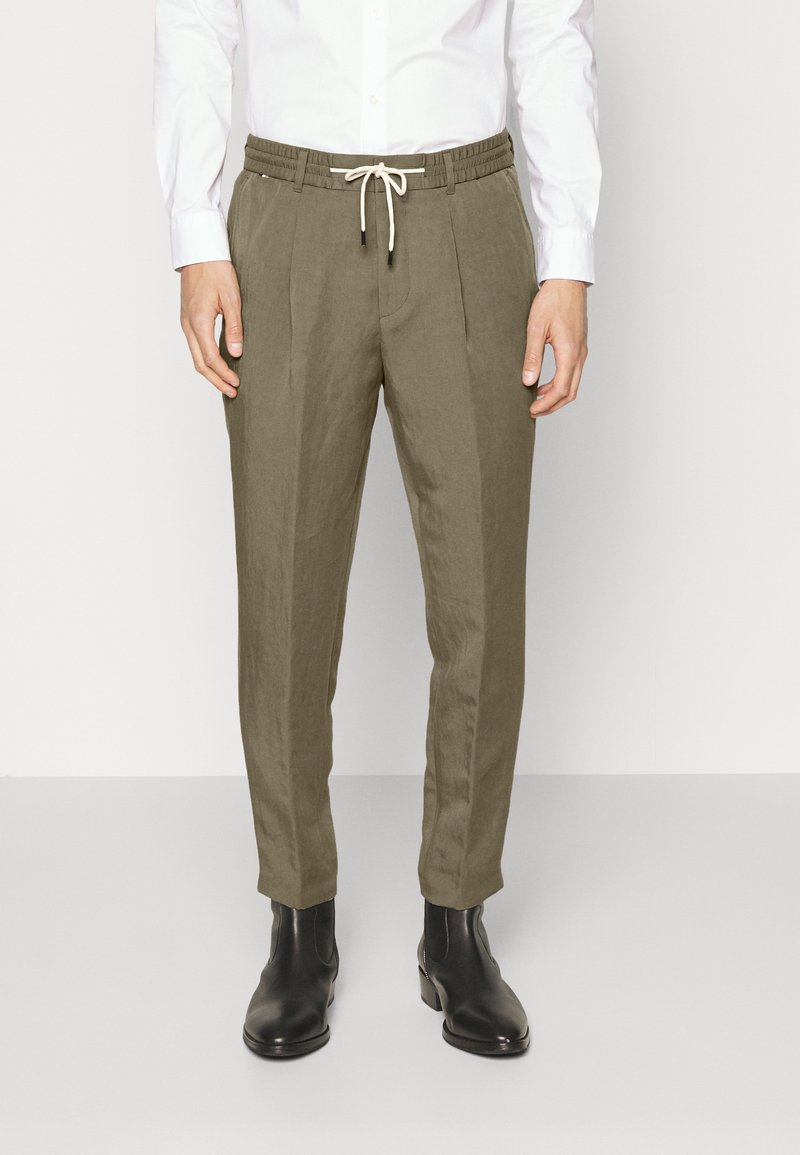 Olive green linen blend trousers with an elastic waistband and drawstring, featuring side pleats, tapered fit, and ankle-length cut.