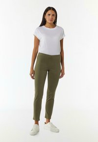 Witte t-shirt met korte mouwen, gecombineerd met olijfgroene slim fit broek en witte sneakers, met een eenvoudig ontwerp en effen kleur.