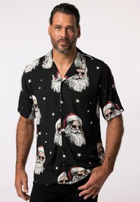 Czarny t-shirt z krótkim rękawem z wzorem czaszki Świętego Mikołaja, zawierającym białe brody i czerwone czapki, akcentowany białymi gwiazdkami. Gładka faktura materiału.