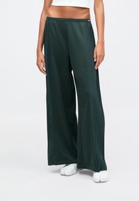 Calças largas verde-escuras feitas de um tecido suave, com pregas nas laterais e um cós elástico. Logótipo da Nike na parte da frente.