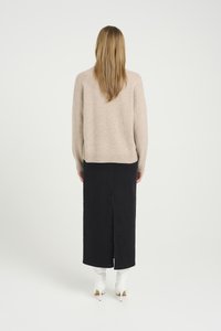 Beige strikket genser med avslappet passform, paret med et svart denimskjørt med en sprekk bak, og hvite hæle ankle boots.