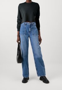 Pullover nero a maniche lunghe tagliato, jeans blu a vita alta e ampi, e borsa nera a spalla con base piatta. Tessuto morbido e vestibilità rilassata.