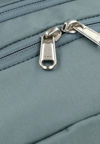 Helles blaues Gewebe mit zwei Metall-YKK-Reißverschlüssen mit eleganten Zippern und sichtbaren Nähten, das eine glatte Textur und ein praktisches Design zeigt.