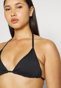 Top de bikini preto em forma de triângulo com alças finas ajustáveis e tecido franzido na base; textura suave e design clássico.
